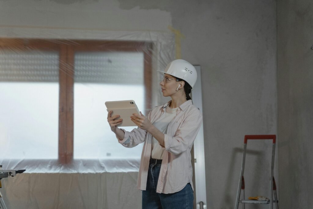 A female architect wearing a hard hat uses a tablet on a construction site for interior design planning.